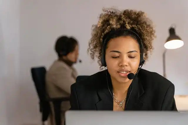 Customer service representative wearing a headset and black blazer while working at a desk.