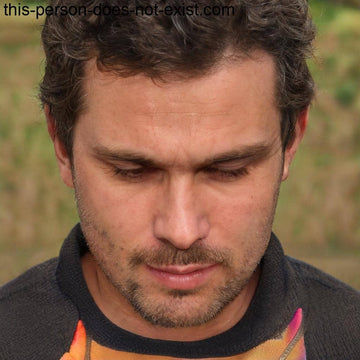 A man with dark, curly hair and a neatly trimmed beard, looking downwards with a serious expression.