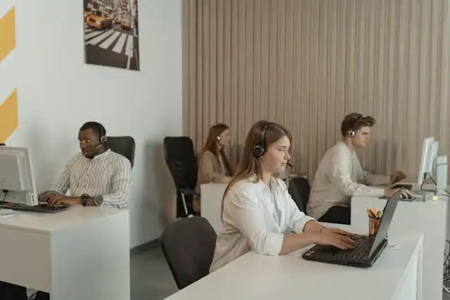 Modern office workspace with people working at white desks using computers.