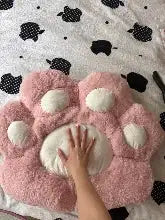Pink plush paw-shaped cushion with white padded pads and a soft, fluffy texture.