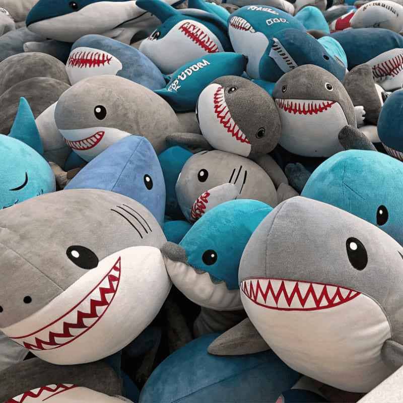 Shark plush toy with large teeth and smiling face, made of soft fabric in shades of gray and blue.